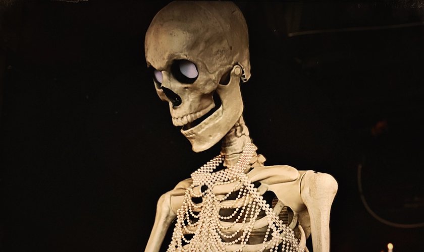 A skeleton draped in strands of pearls beside a candelabra